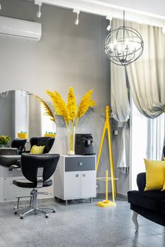 Modern small bright hair and beauty salon in black and yellow colors with gray walls and floor and black sofa with yellow cushions