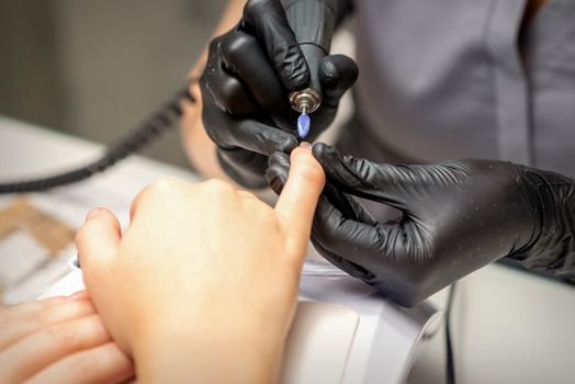 Manicure master uses electric nail file machine in a nail salon, close up