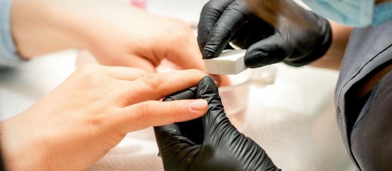 Close up of the caucasian hands of a professional manicurist are filing the nails of a young woman. Young caucasian woman receiving a manicure by a beautician with a nail file in a nail salon