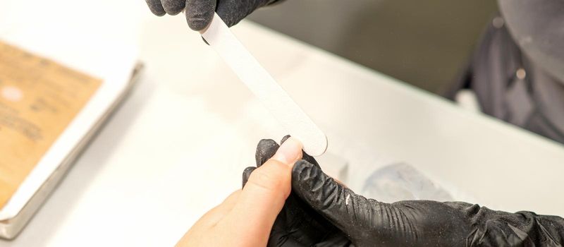 Close up of the caucasian hands of a professional manicurist are filing the nails of a young woman. Young caucasian woman receiving a manicure by a beautician with a nail file in a nail salon