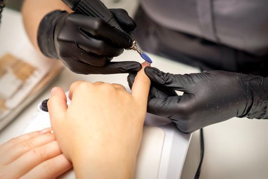 Manicure master uses electric nail file machine in a nail salon, close up