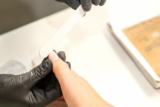 Close up of the caucasian hands of a professional manicurist are filing the nails of a young woman. Young caucasian woman receiving a manicure by a beautician with a nail file in a nail salon