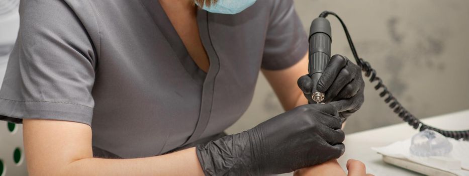 Manicurist removes nail polish uses the electric machine of the nail file during manicure in a nail salon