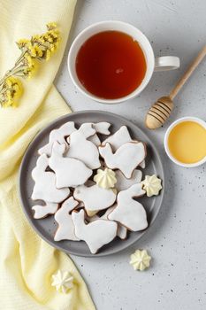 Easter cookies in the form of a rabbit on a gray plate with yellow textiles, a cup of tea and honey on a gray background. vertical photo