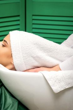 Hairdresser wraps hair of a young caucasian woman in a white towel after washing head in the hairdressing salon