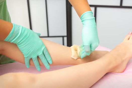 Waxing depilation procedure for removing hair on legs with sugaring paste in the beauty salon