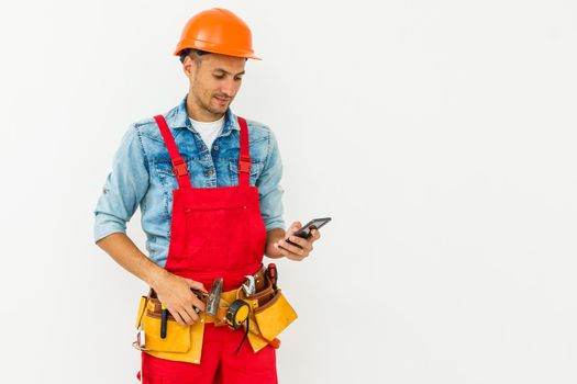 profession, construction and building - happy smiling male worker or builder in helmet and overall with smartphone over white background.