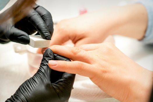 Close up of the caucasian hands of a professional manicurist are filing the nails of a young woman. Young caucasian woman receiving a manicure by a beautician with a nail file in a nail salon