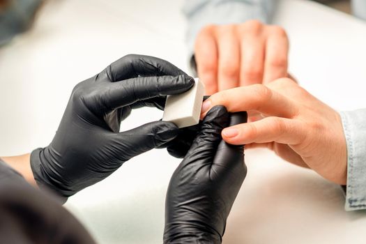 Close up of the caucasian hands of a professional manicurist are filing the nails of a young woman. Young caucasian woman receiving a manicure by a beautician with a nail file in a nail salon