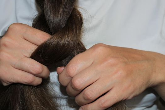 A girl with long dark hair is braiding her hair. Close-up hands. Hair care. Hair loss problem.