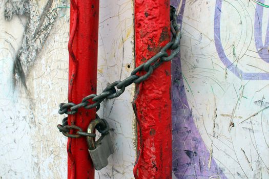 An old padlock on a rusty chain wrapped around red pipes.