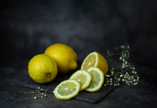 winter still life with a cut bright yellow lemon and gypsophila flowers lying next to them on a table on a dark background High quality photo