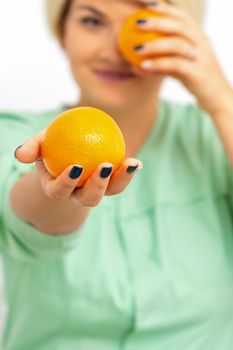 Smiling female nutritionist holding a whole orange, offering and looking at camera over white background, healthy diet concept