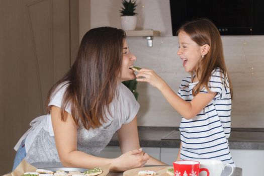 A little girl feeds her mother with cooked cookies in the kitchen. Real life. The concept of cooking with children.