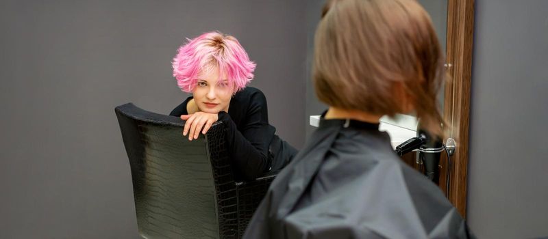 Portrait of a beautiful young caucasian woman with a new short pink hairstyle sitting in a chair at a hairdresser salon