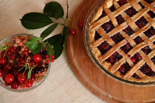 Top view of classic American festive cherry pie with crispy sweet pastry lattice and fresh ripe organic berries in bowl. Homemade berry cake with flaky crust. Thanksgiving concept. Bakery products