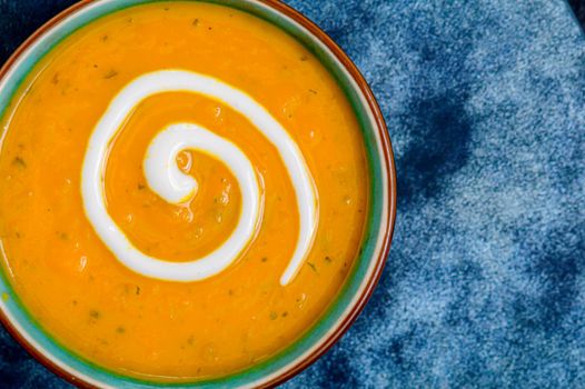 Autumnal spiced carrot and coriander soup with a swirl of cream on blue and black tabletop