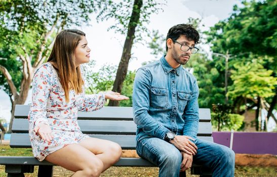 Upset couple arguing in a park. Girl arguing with her boyfriend sitting in a park, Young couple arguing and complaining sitting on a park bench, Concept of couple problems and jealousy
