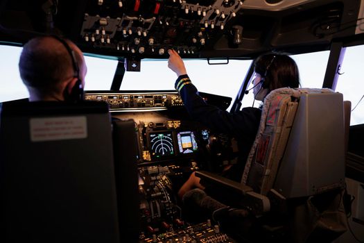 Female pilot assisting captain to takeoff and fly airplane, using buttons on dashboard command in pilot cockpit. Airliners flying plane jet with navigation windscreen and control panel.