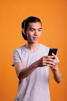 Young asian man typing message on smartphone, online communication concept. Cheerful teenager standing, browsing internet on mobile phone, attractive person using social media