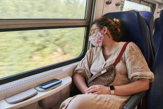 A girl with glasses in a medical mask sleeping on the train. High quality photo