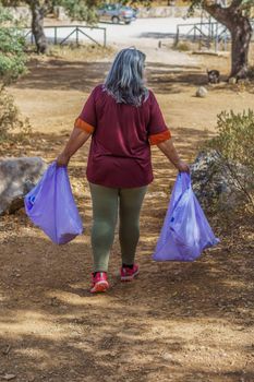 woman seen from the back carrying bags of garbage collected in the field