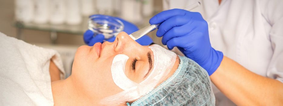 Face peeling at the beautician. Facial treatment. The beautician applies a cleansing face mask to the female patient