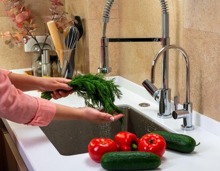 Girl washes herbs and vegetables for salad.