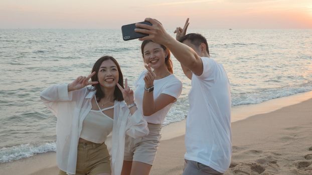 Happy friends smiling and posing taking selfie from smartphone and having fun together on beach in holiday vacation time at sunset, Young Asian group woman and man in summer travel outdoor