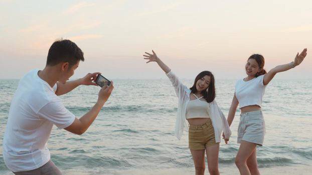 Happy friends smiling and posing taking photo from smartphone and having fun together on beach in holiday vacation time at sunset, Young Asian group woman and man in summer travel outdoor