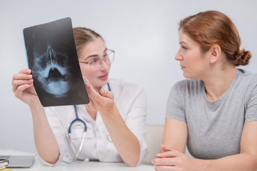 A woman doctor and a patient at the reception are discussing an x-ray of the sinuses