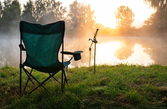 Fisherman's chair and fishing rods in the background over the lake at sunrise, foggy morning. Fishing concept