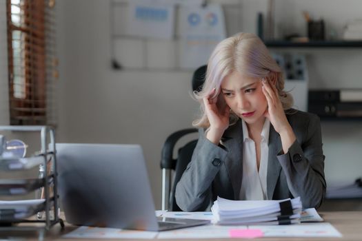 Stressed Asian businesswoman analyzes financial charts. Account and audit concept.