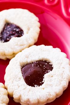 Linzer Torte cookies on red plate with powdered sugar sprinkled on top.