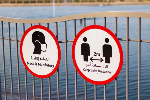 Covid 19 warning signs in Arabic and English languages on the fence of the park.