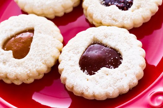 Linzer Torte cookies on red plate with powdered sugar sprinkled on top.