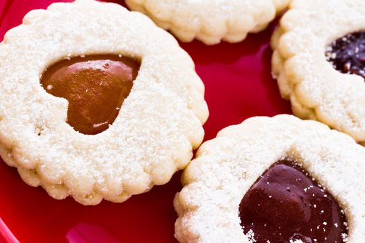 Linzer Torte cookies on red plate with powdered sugar sprinkled on top.