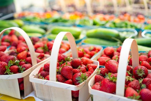 Strawberries for sale on vegetables market. Raw juicy strawberry in wooden basket standing on market display with other fruit and berry on background. Seasonal sweet berry