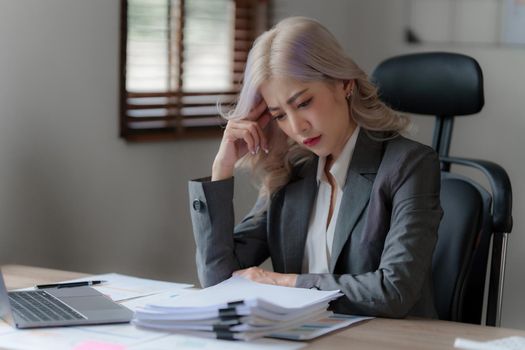 Stressed Asian businesswoman analyzes financial charts. Account and audit concept.