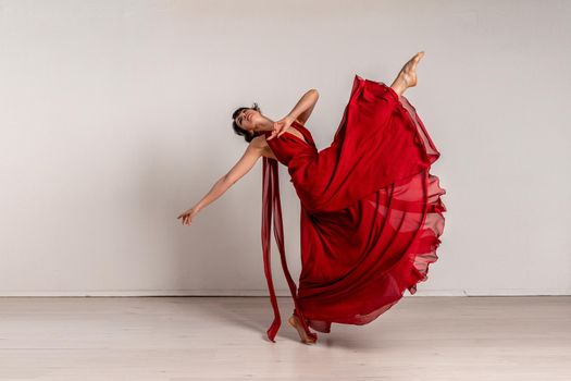 Dancer in a red flying dress. Woman ballerina dancing on a white studio background.