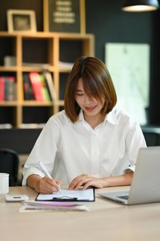 Portrait of successful entrepreneur using laptop computer and doing some paperwork at her office.