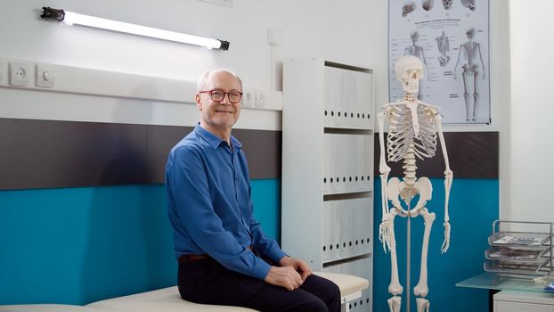 Portrait of elderly man waiting to attend checkup visit with physician in medical office, having consultation appointment at healthcare facility. Oold patient sitting in cabinet to do examination.