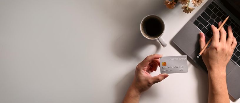 Overhead view of woman holding credit card and making payment on internet via laptop. Online shopping, e-commerce concept.