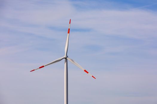 A red and white three-propeller wind turbine against the blue sky