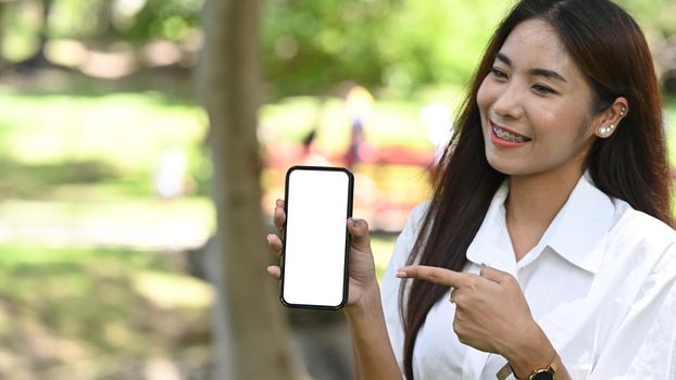 Smiling young woman holding mock up smart phone with blank screen.