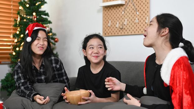 Three asian children sitting near Christmas tree at home.