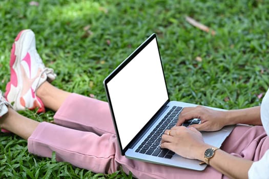 Cropped shot young woman sitting on grass in the park and working with computer laptop.