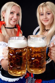 Young and beautiful bavarian girls with two beer mugs on black background. Oktoberfest
