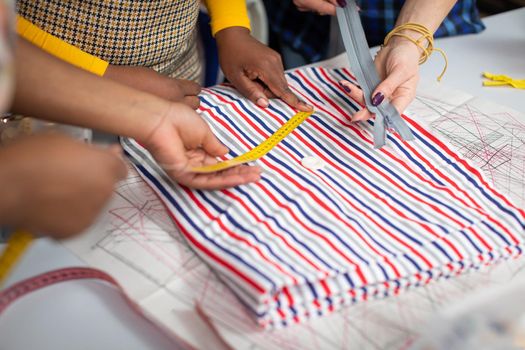 A dark-skinned girl measures a piece of colorful striped fabric with a tailor's centimeter. The process of measuring fabric just before cutting.