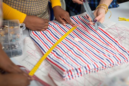 A dark-skinned girl measures a piece of colorful striped fabric with a tailor's centimeter. The process of measuring fabric just before cutting.